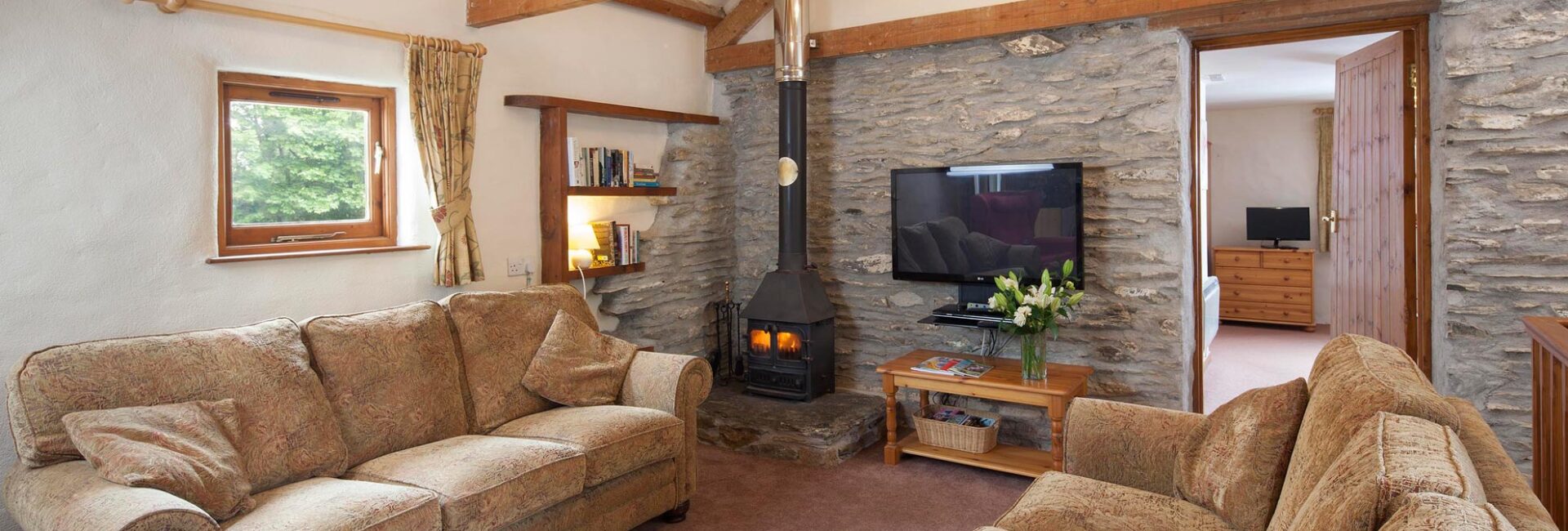 Inside Valley View showing exposed beams, flat screen TV and wood burner.