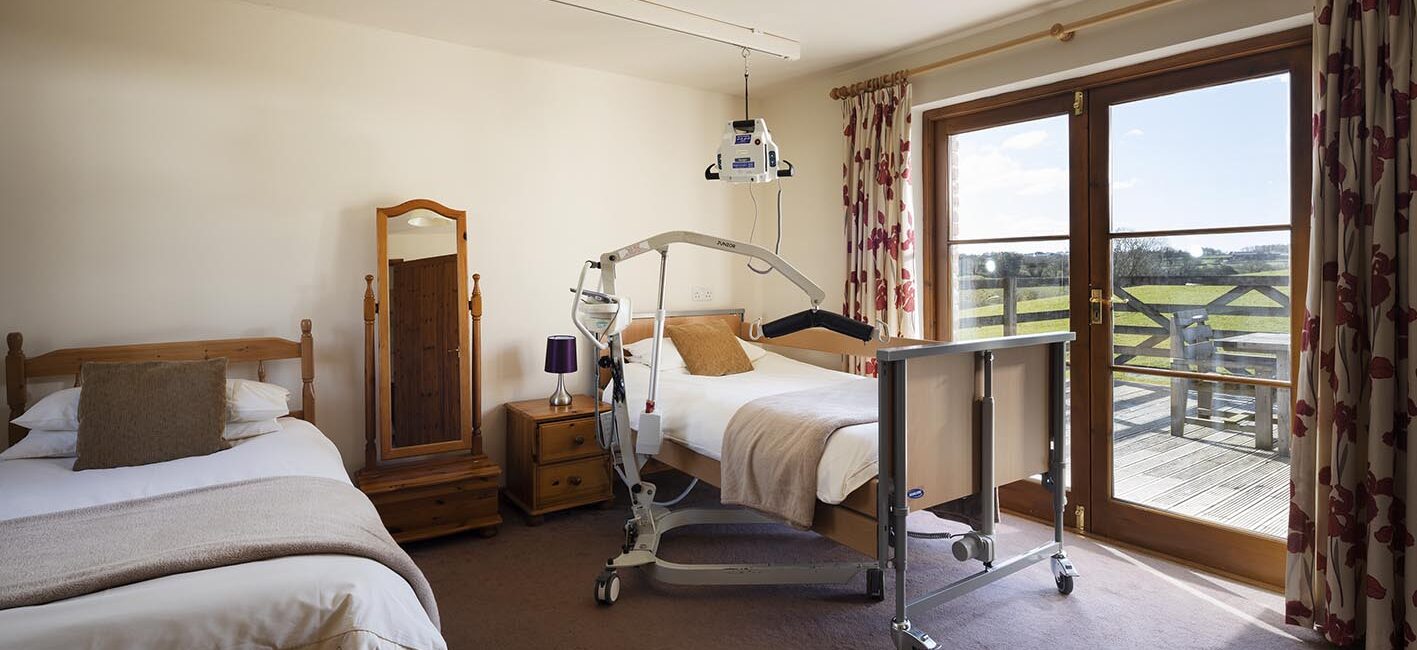 Buzzard Watch accessible bedroom with ceiling hoist or portable hoist, electric profiling bed and level access out to the patio area through french doors at Treworgans Farm Holidays wheelchair accessible holiday cottages.