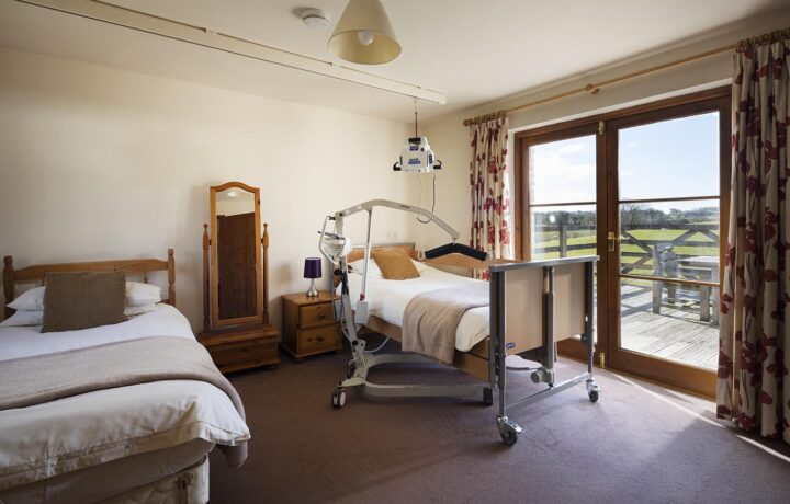 Buzzard Watch accessible bedroom with ceiling hoist or portable hoist, electric profiling bed and level access out to the patio area through french doors at Treworgans Farm Holidays wheelchair accessible holiday cottages.