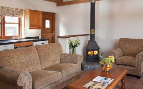 The open plan sitting room in Buzzard Watch with sofas, electric riser recliner chair and woodburner